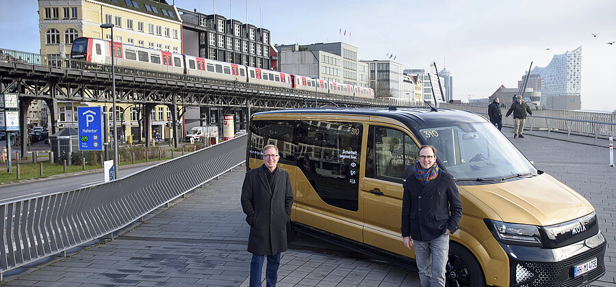 Ein Kleinbus mit zwei Personen vor der Kulisse der Hamburger Hochbahn